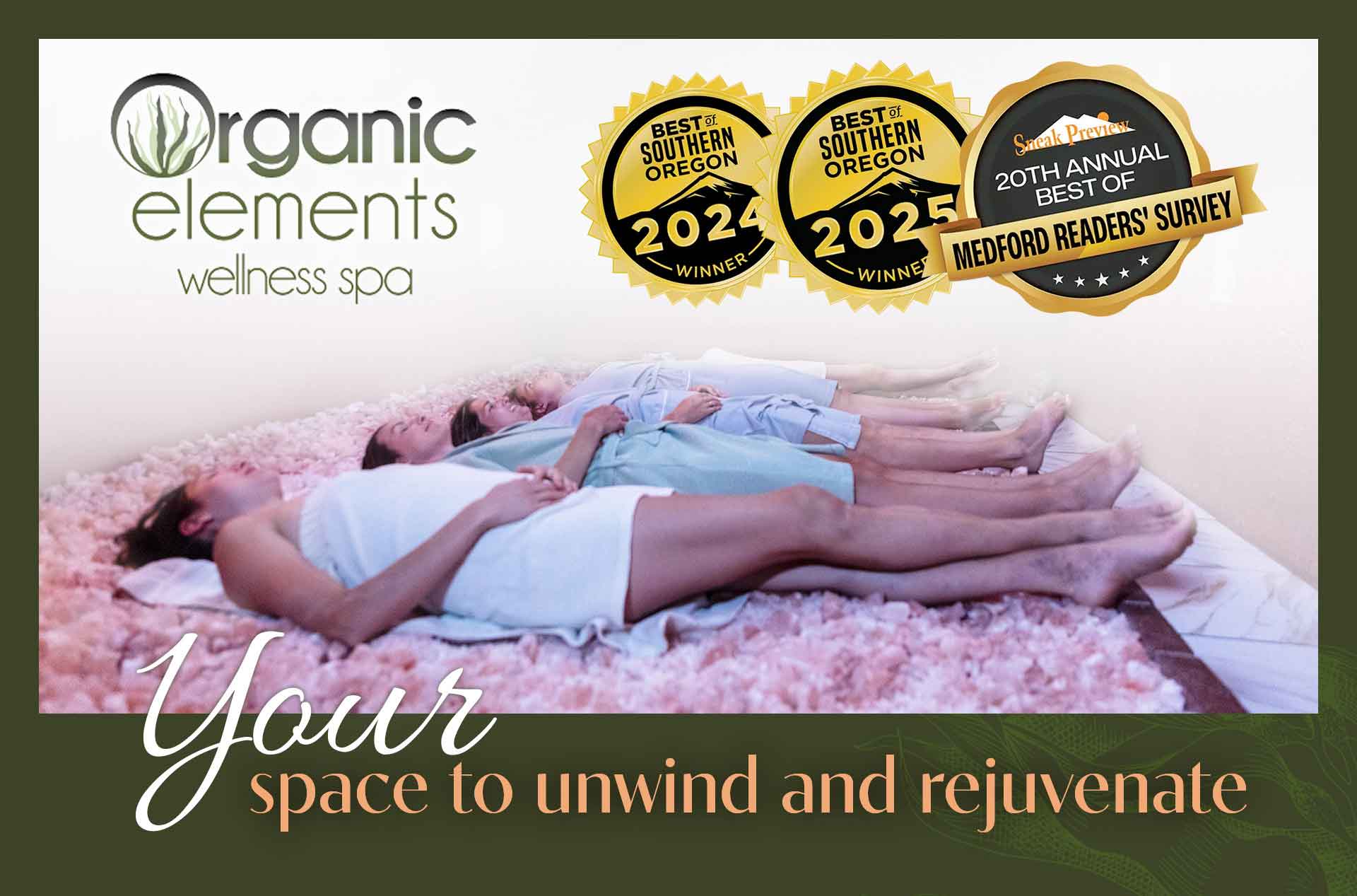 Three people lie side by side on a pink salt bed in a wellness spa, wrapped in light robes and resting with eyes closed. Text reads "Organic Elements wellness spa" and "Your space to unwind and rejuvenate" with award badges for "Best of Southern Oregon 2024 Winner," "2025 Winner," and "20th Annual Best of Medford Readers' Survey."