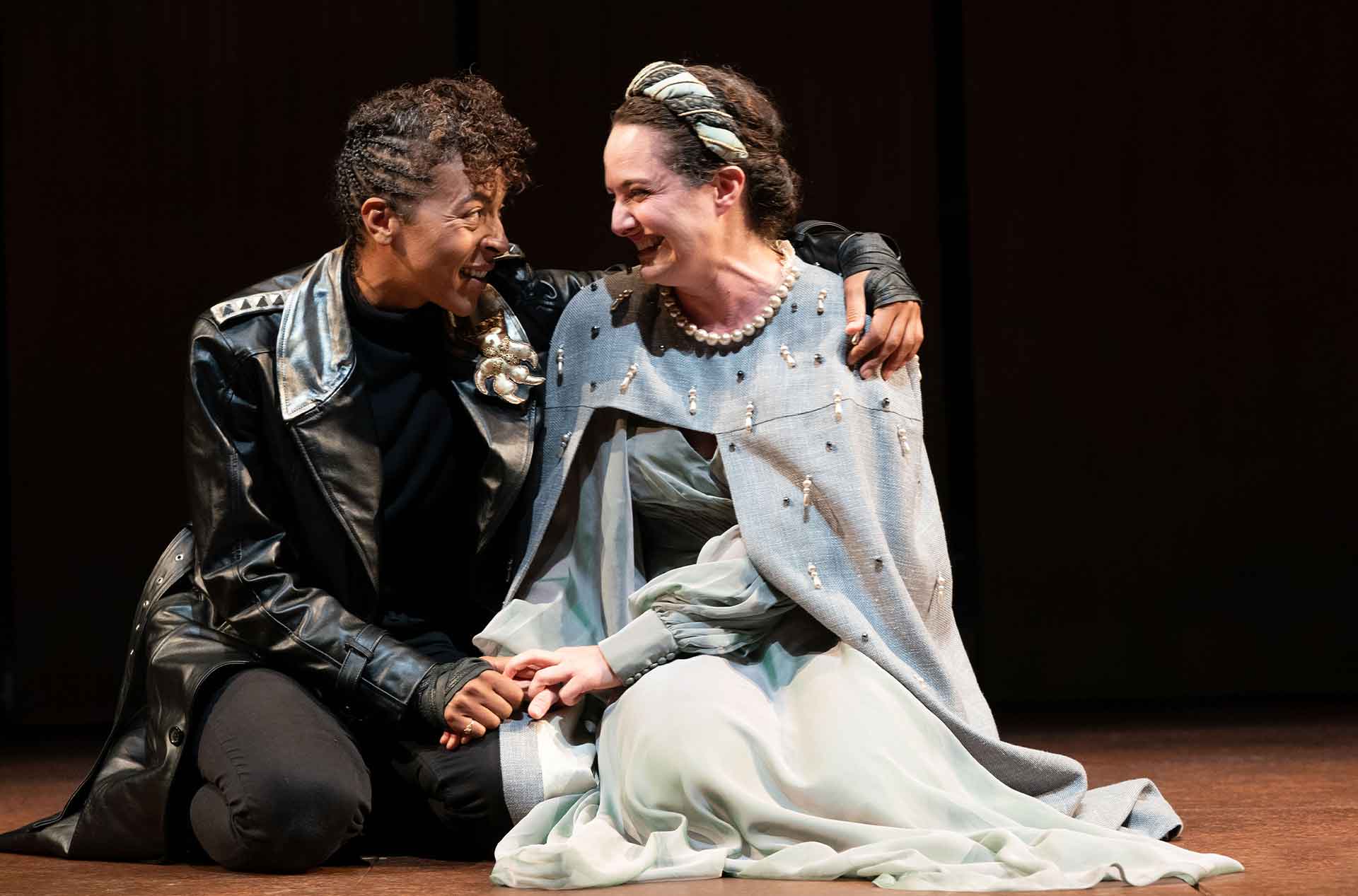 Two people sitting on their knees, looking at each other, and holding hands.