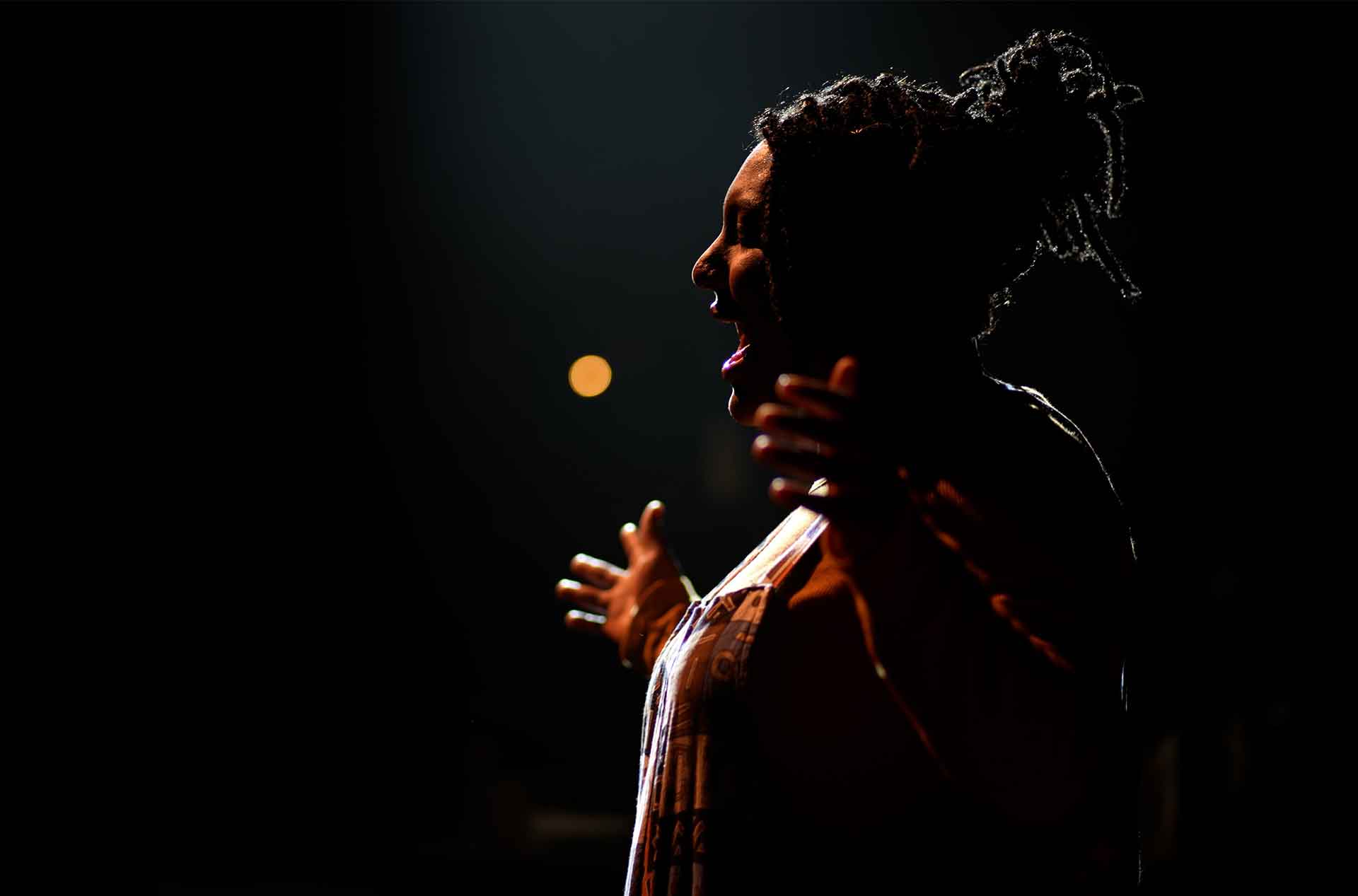 A person standing, singing with arms spread wide open.