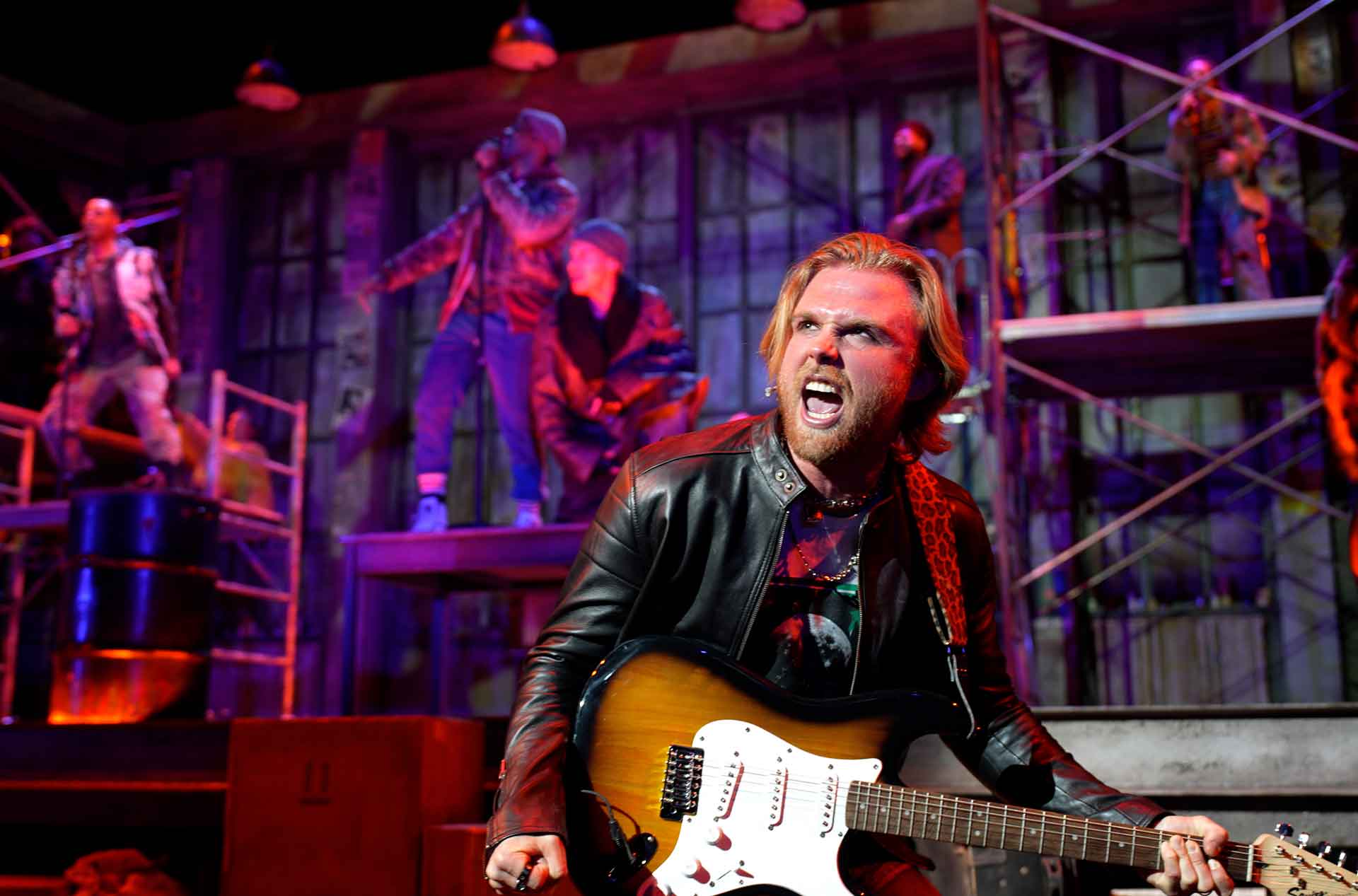 A person singing and playing guitar on stage.