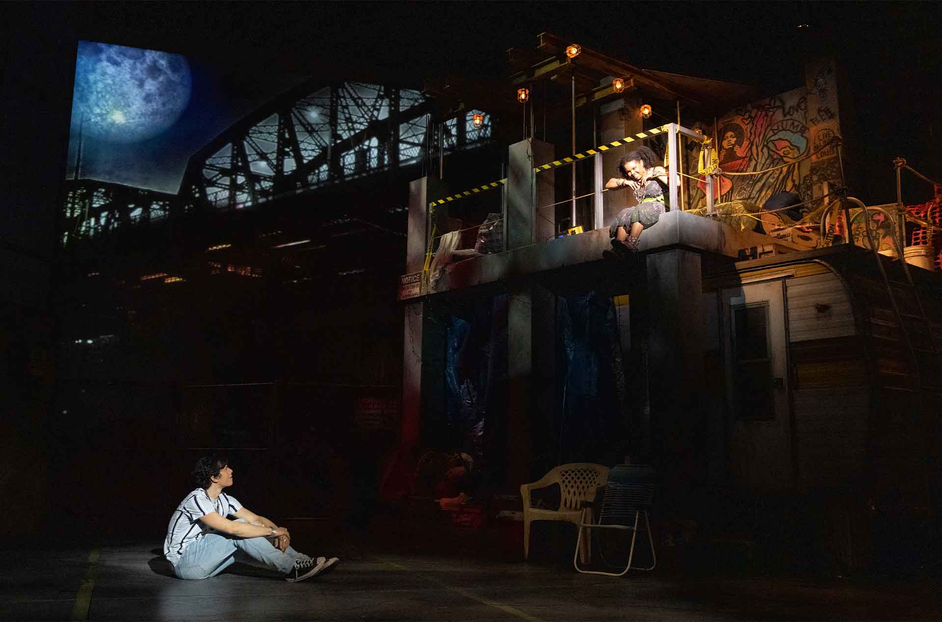 Romeo sitting on ground looking at Juliet on a balcony.