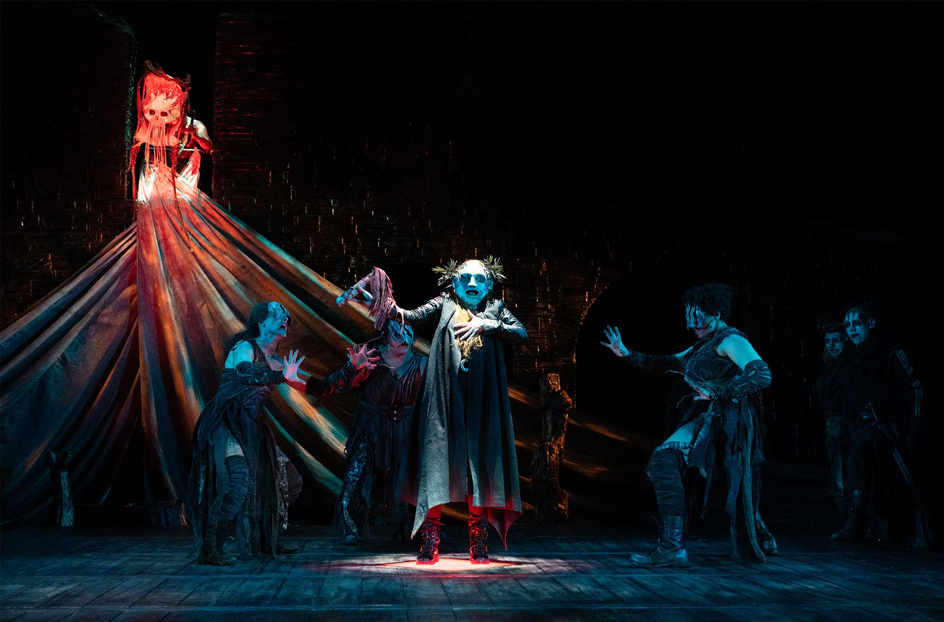 Witches dancing around a person wearing a mask decorated with twigs