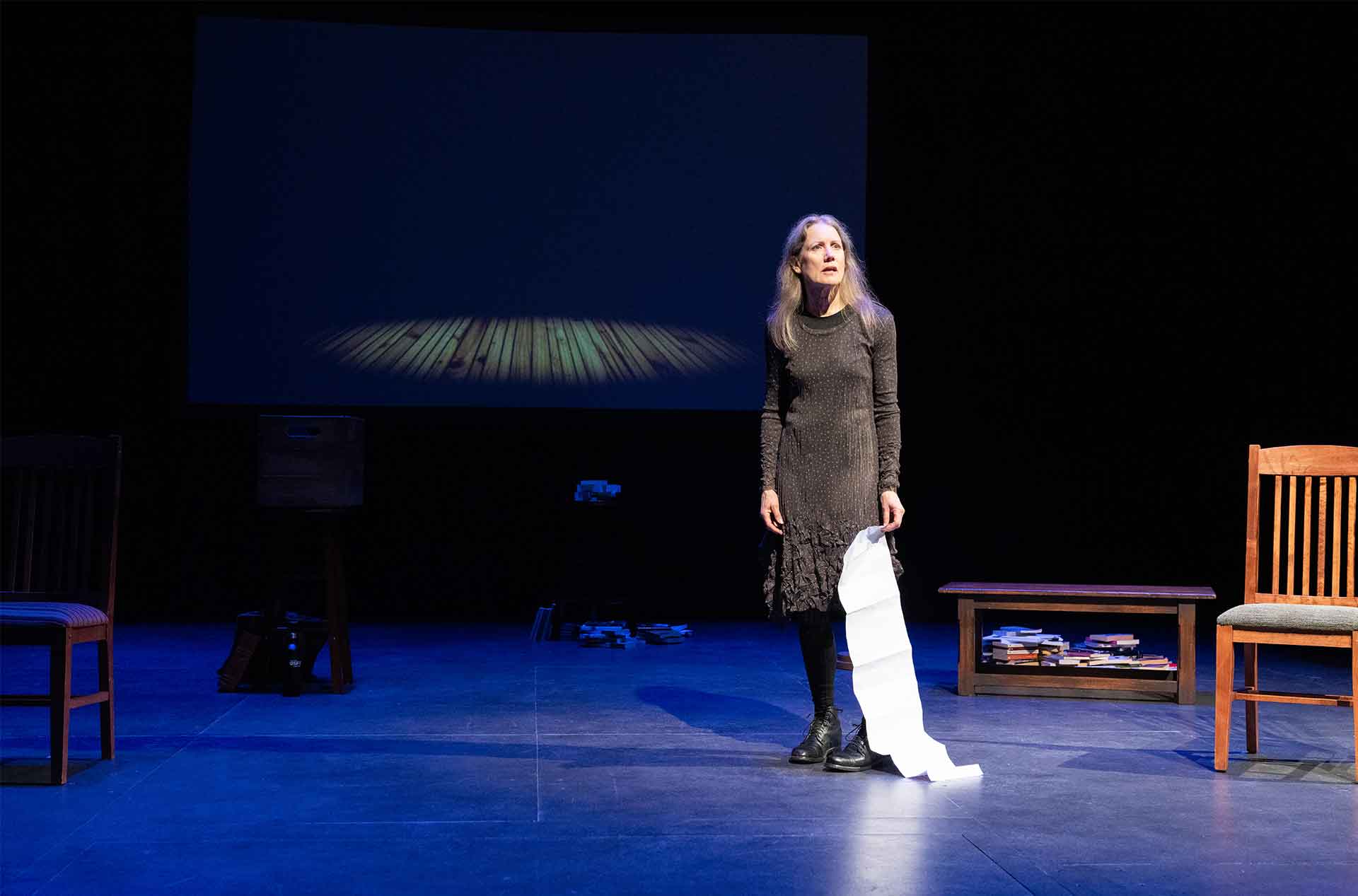A woman standing holding a long paper looking out into the distance.