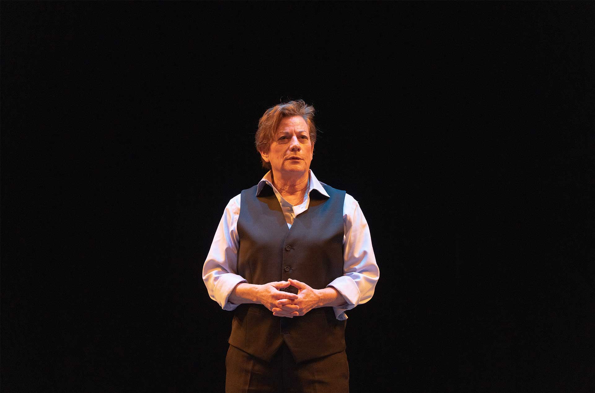 A person standing before a dark background holding their hands at their stomach.