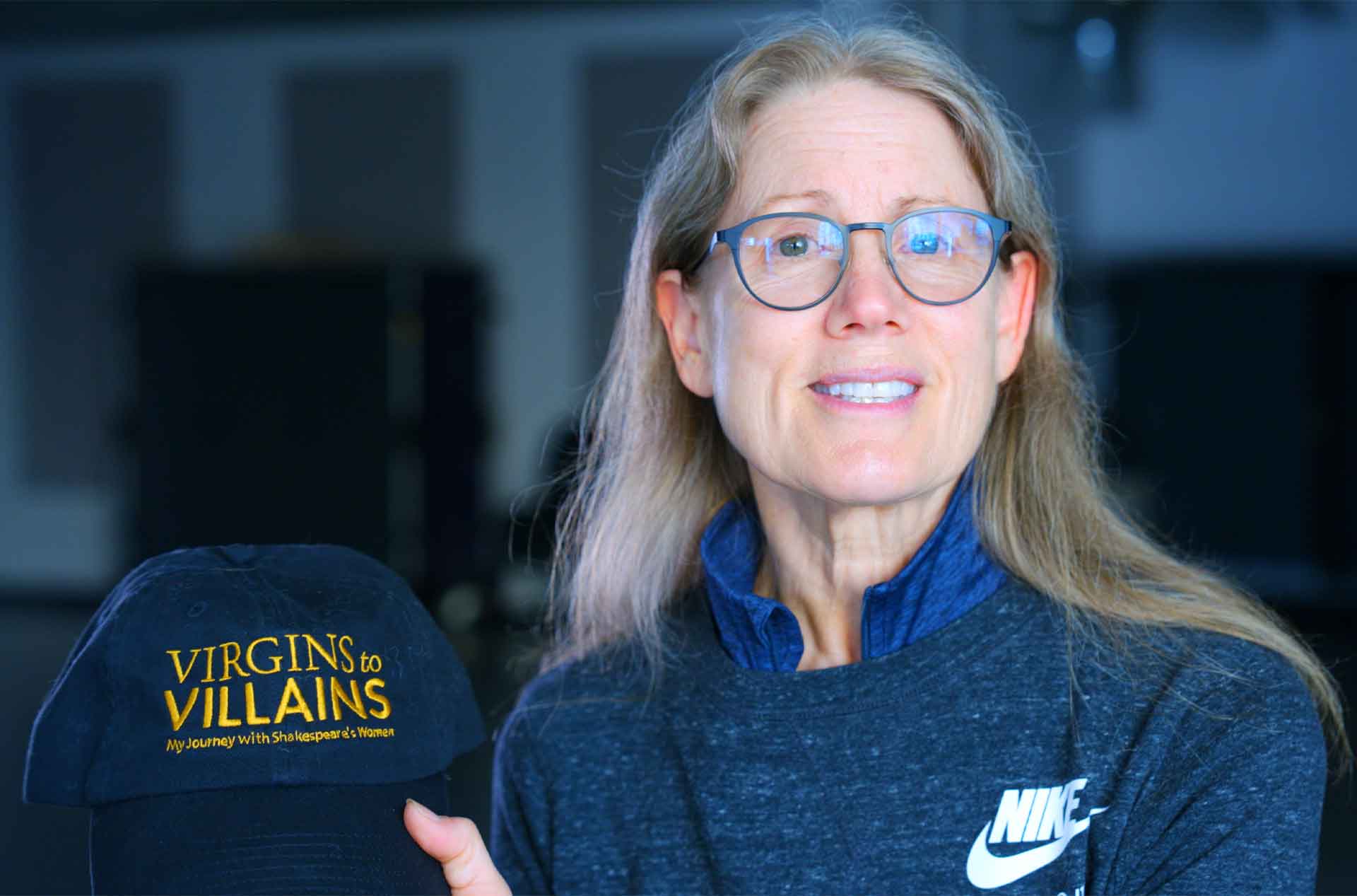 A person wearing glasses holding a hat that says Virgins to Villains.