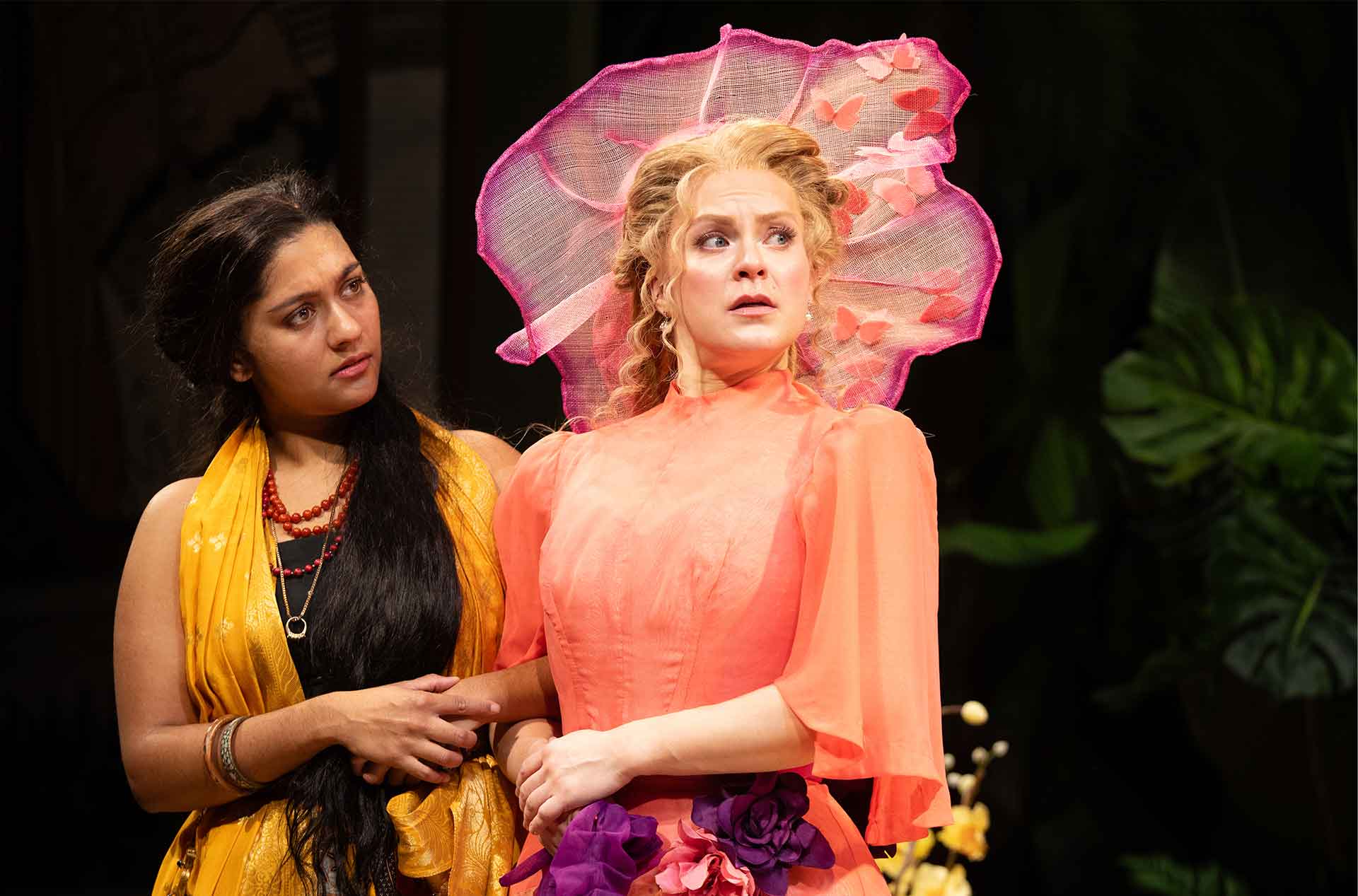 Two characters stand side by side, one appearing concerned while the other looks shocked, wearing a large, decorative hat.