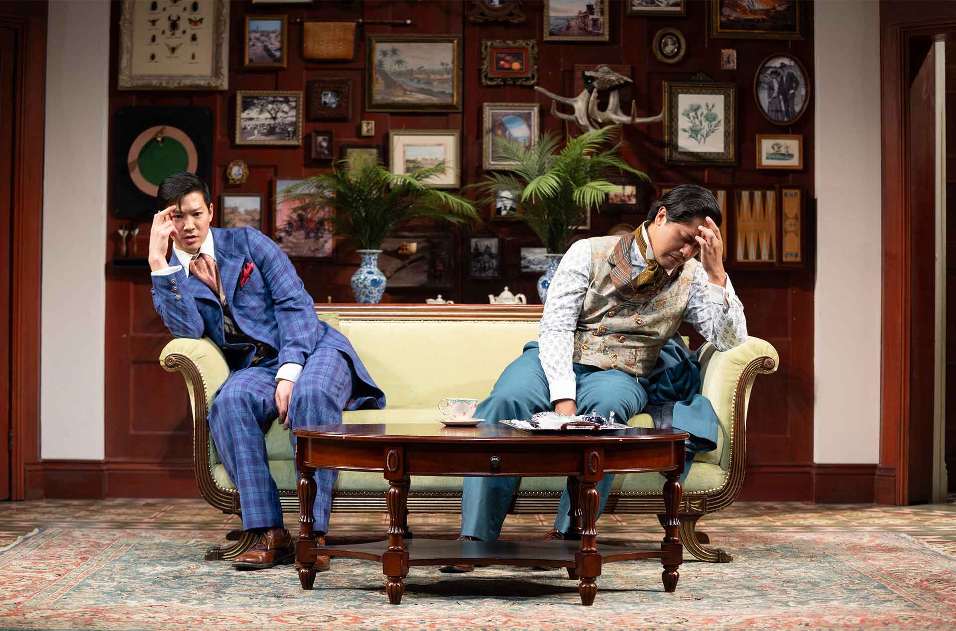 Two individuals sit on a couch in a lavishly decorated room, both holding their heads in frustration or contemplation.