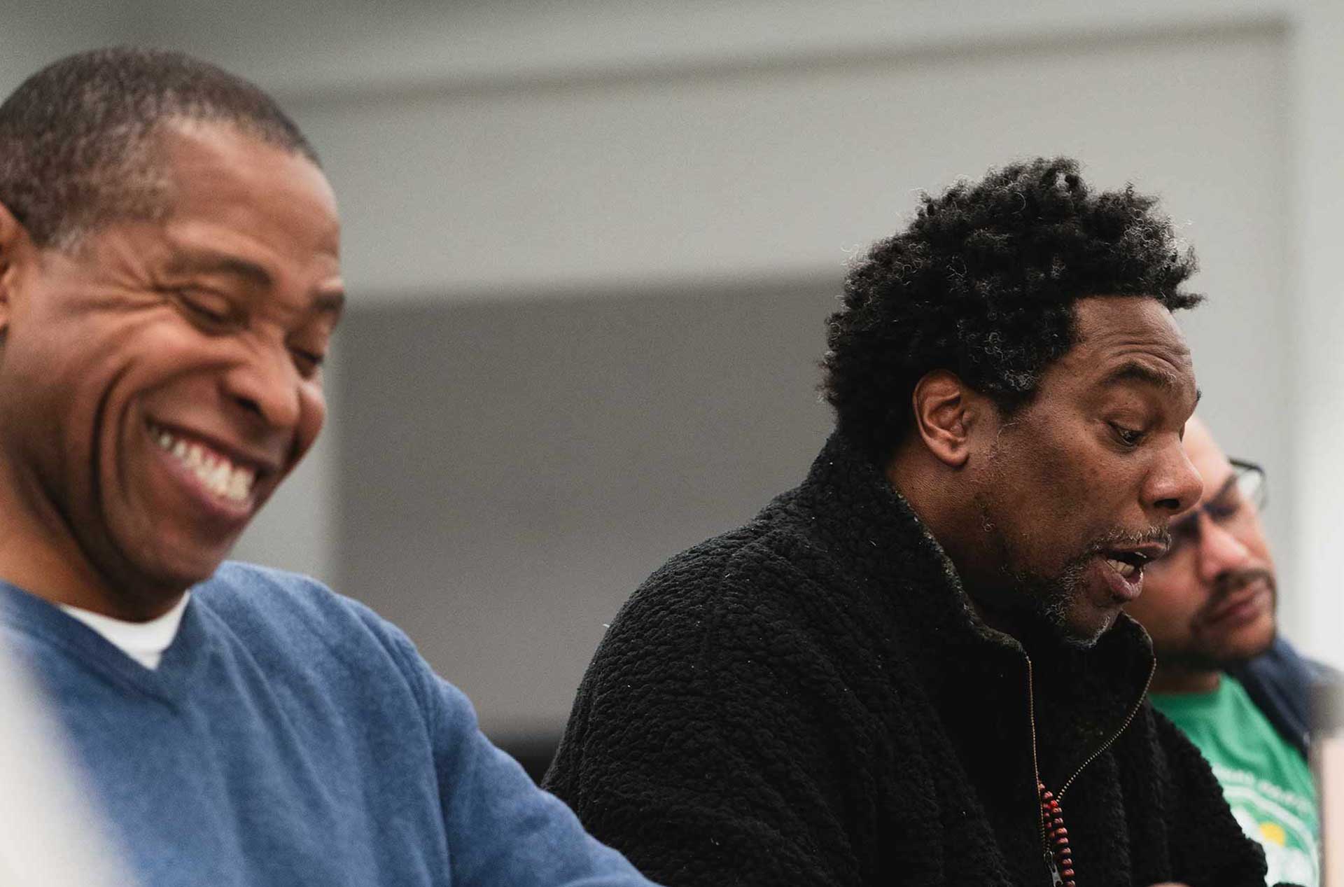 Two people sitting side by side, one smiling brightly while the other speaks animatedly.