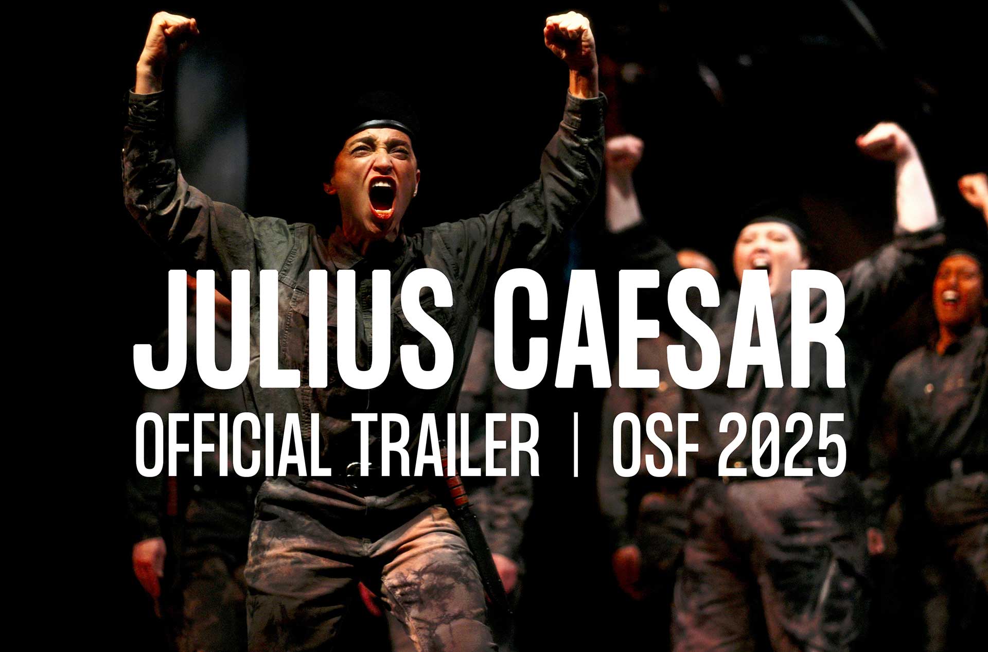 A group of performers in military-style uniforms passionately shout with raised fists on a dark stage, evoking intensity and unity. The central figure is especially expressive, leading the charge with a fierce expression and wide stance.