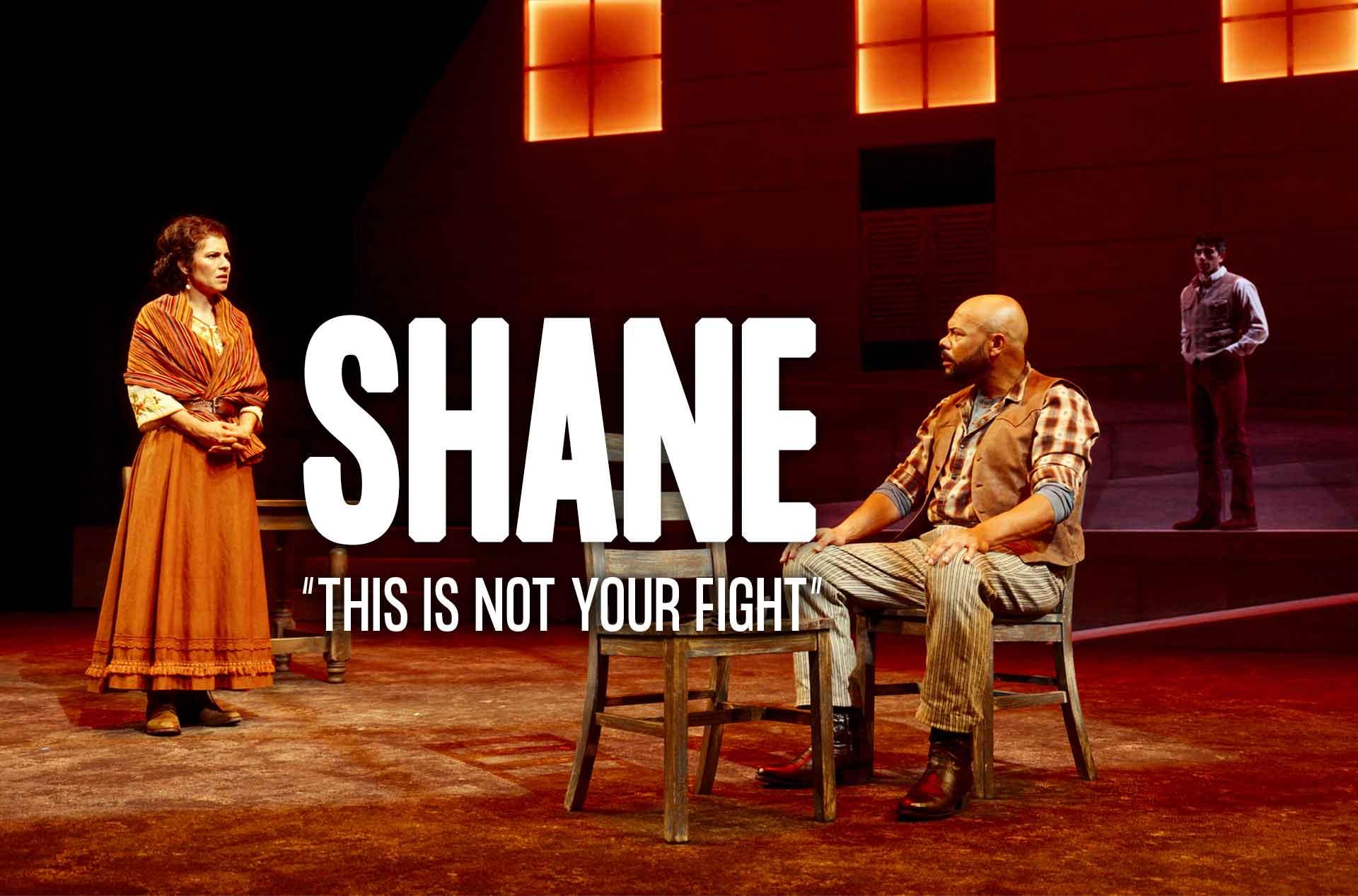 Three actors on stage in a dramatic scene; one stands left, one sits center, one stands right. 'SHANE' and 'THIS IS NOT YOUR FIGHT' text overlay.