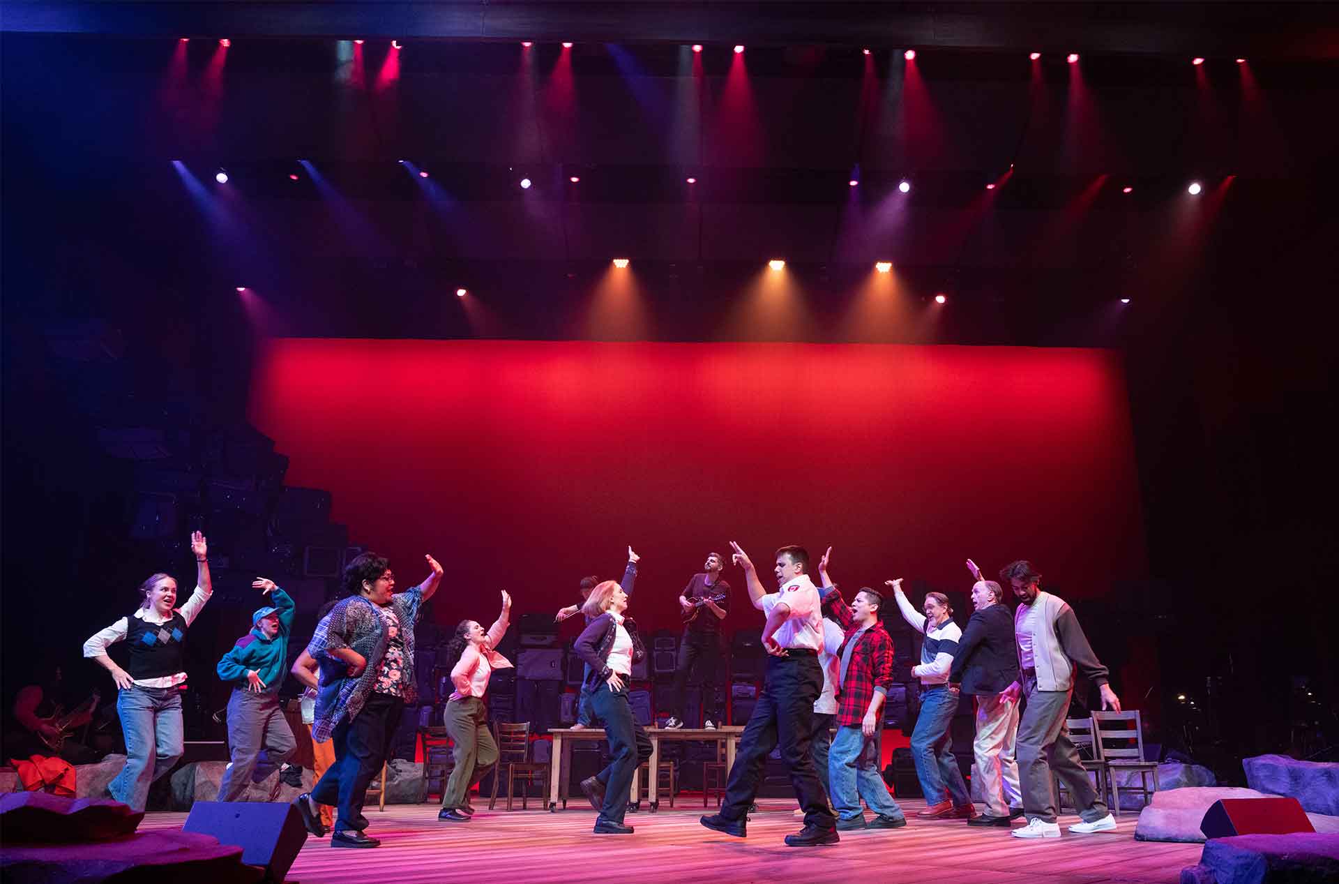 A group of performers dance in unison on stage under red and purple lighting.