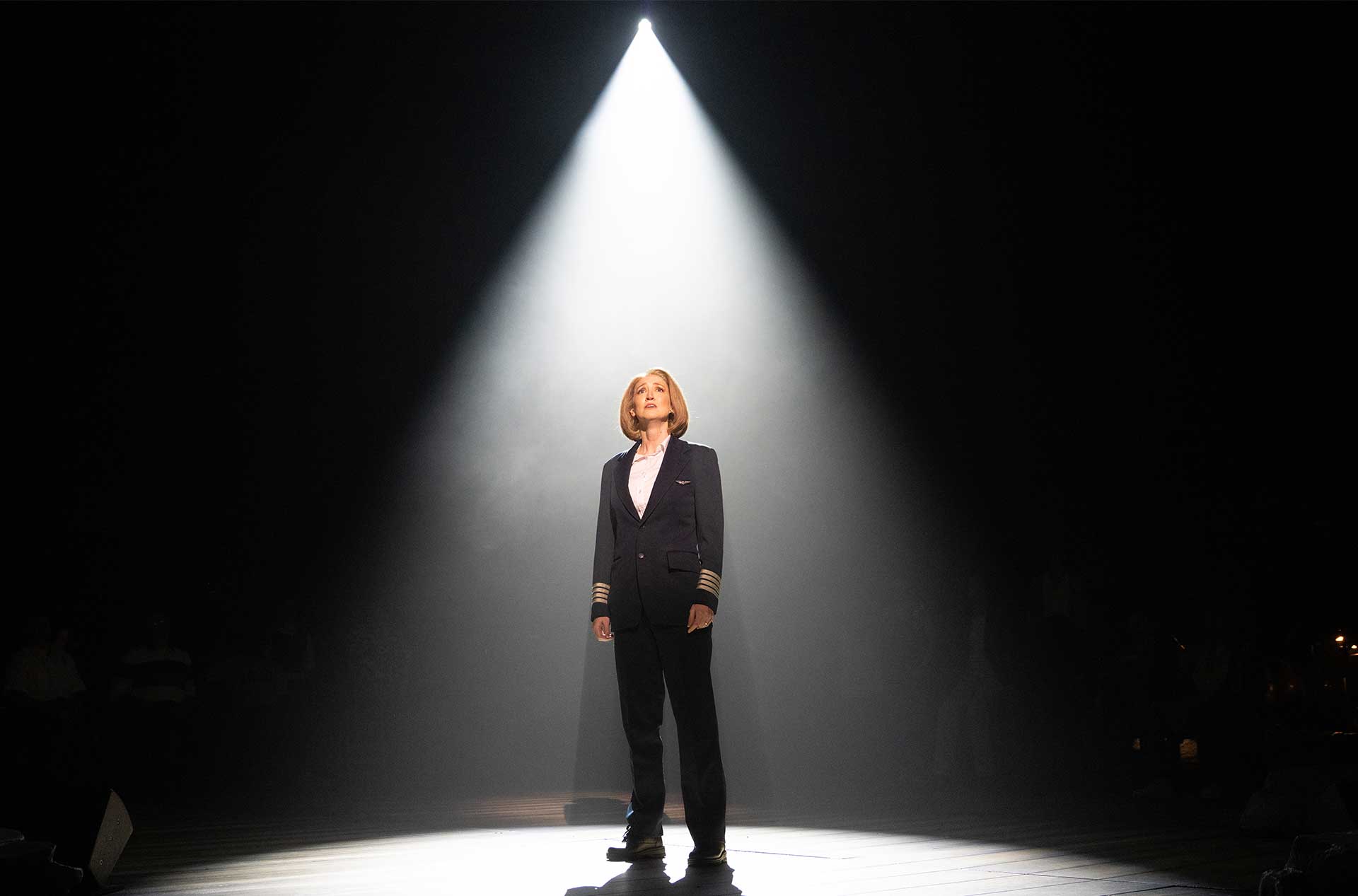 One person stands alone under a spotlight on a dark stage, creating a dramatic isolated moment.