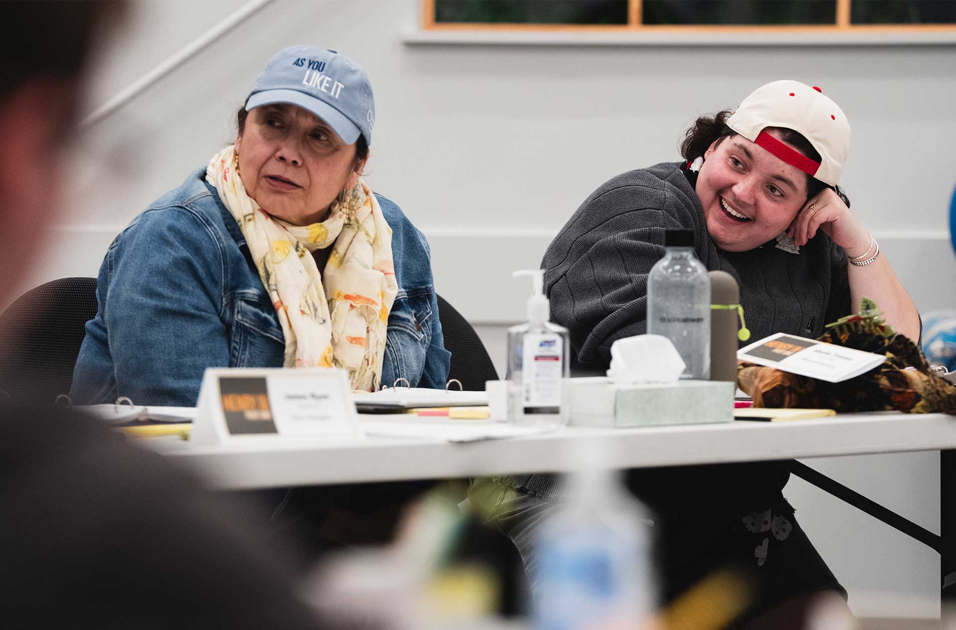 Two people seated at a table smiling and listening during a group discussion.
