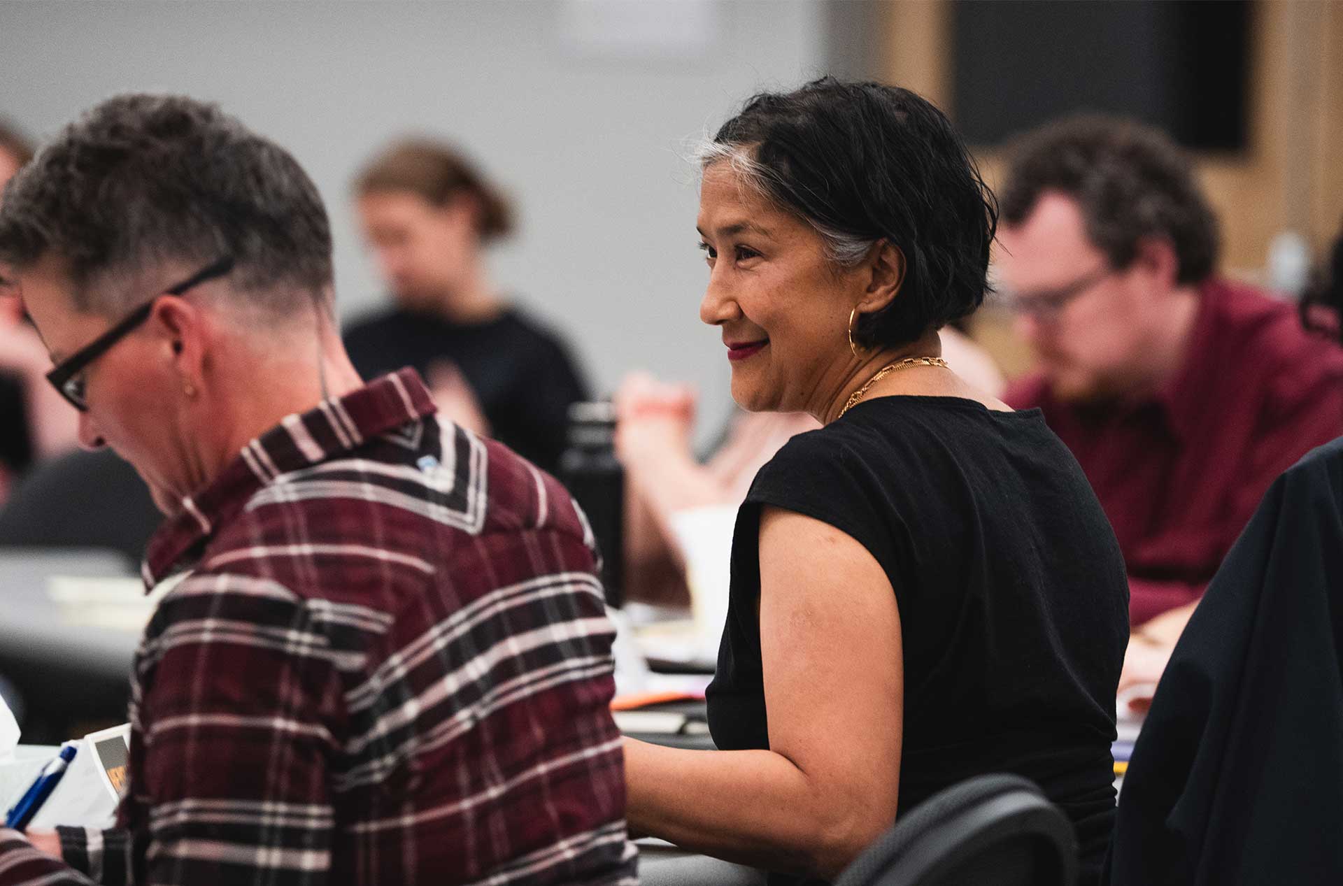 Creative team sit smiling while seated at a table during a play rehearsal.