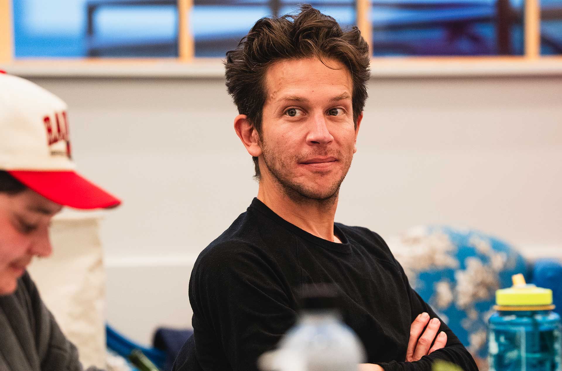 A person smiling with arms crossed during a play rehearsal.