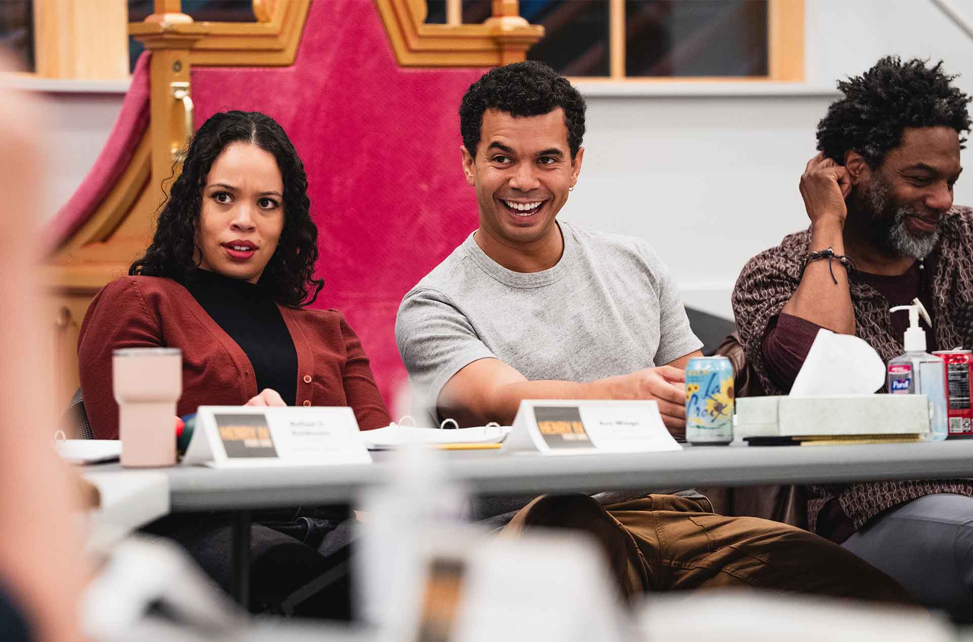 Three people reacting with surprise and laughter during a collaborative discussion around a table.