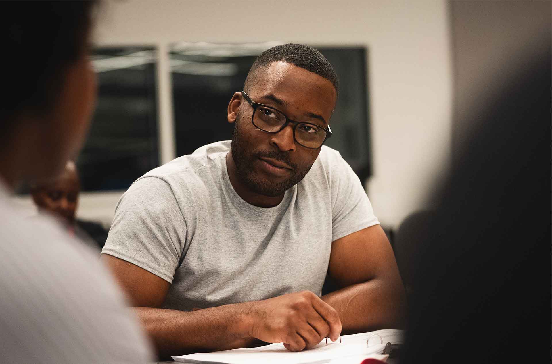Participant in glasses and a t-shirt looking thoughtfully toward someone out of frame during a table read.