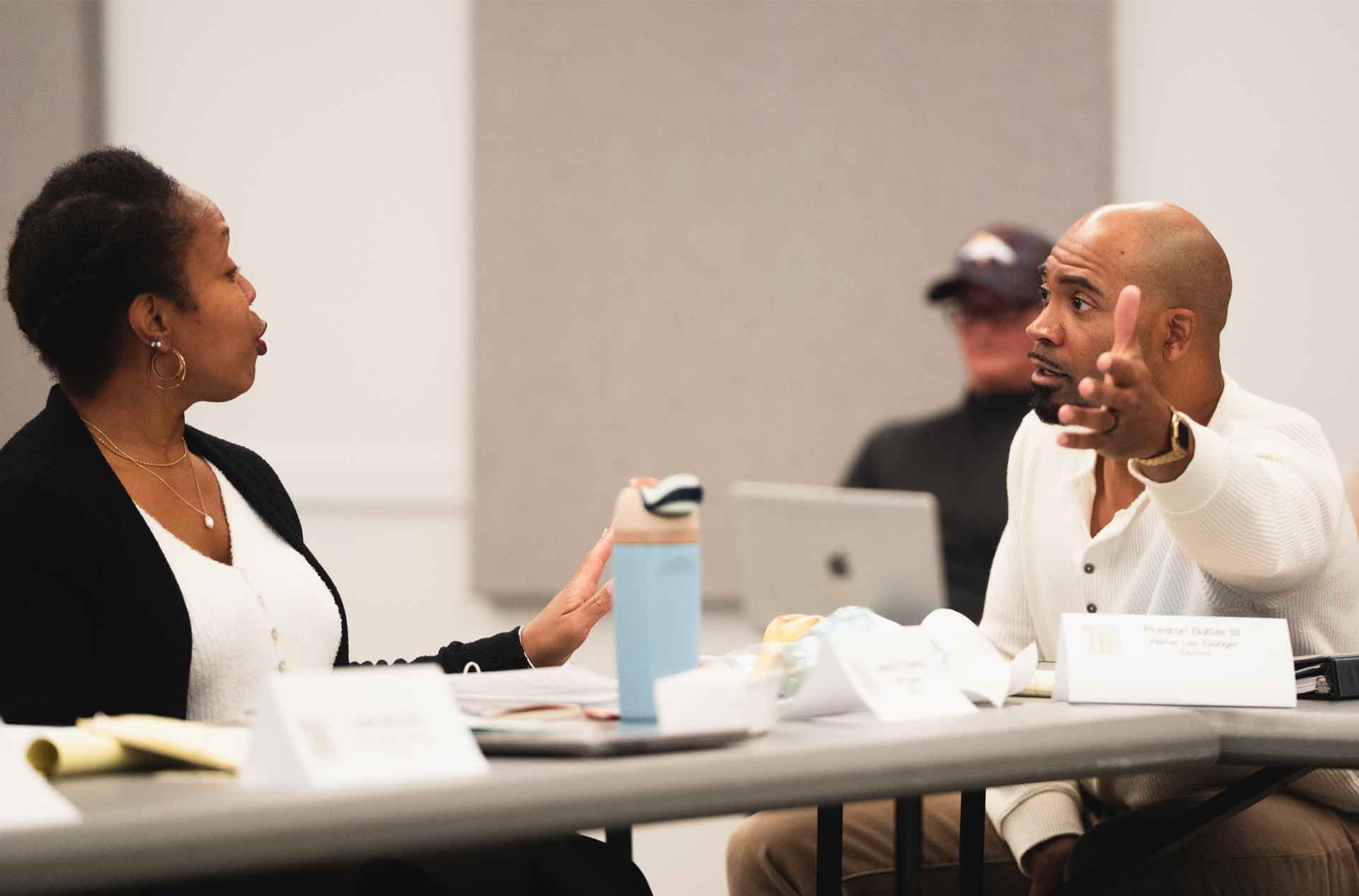 Two people in animated discussion across a table, gesturing expressively during the read-through.