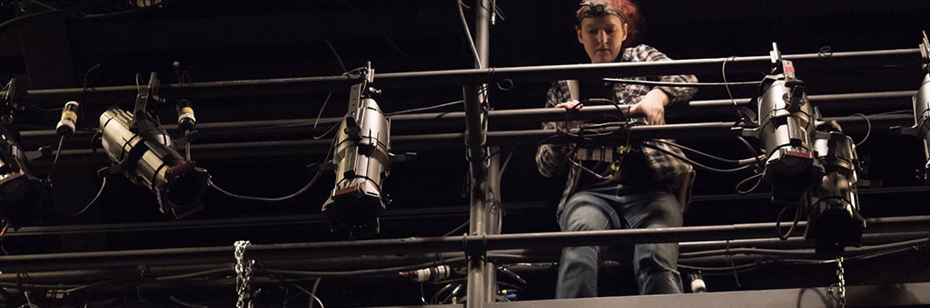 A person standing on scaffolding setting up lights.